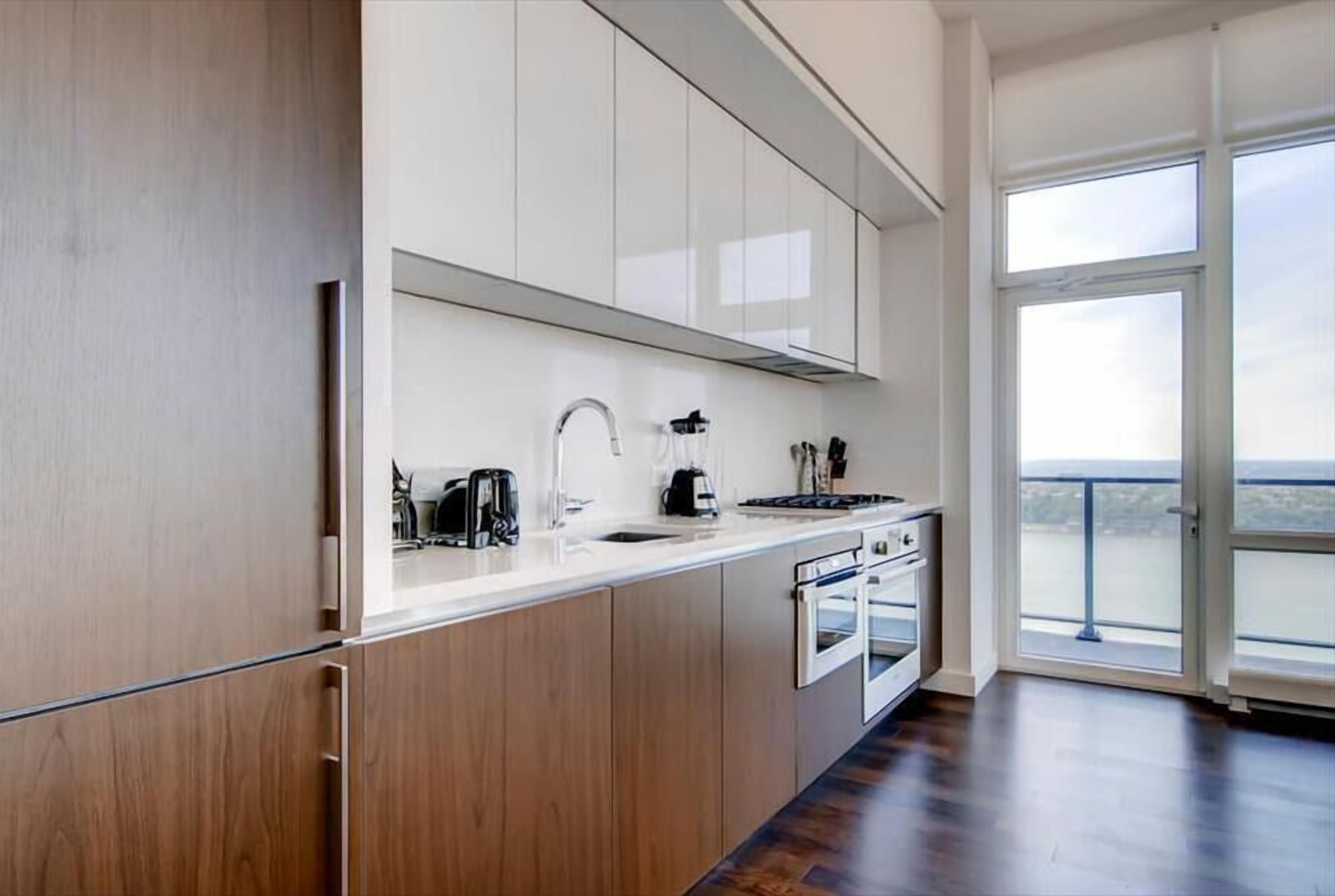 A modern kitchen with white cabinets, stainless steel appliances, and a large window offering a view of the outdoors.