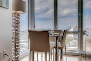 Un comedor con una mesa y sillas, una lámpara y vistas de la ciudad a través de amplias ventanas.