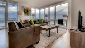 Ein modernes Wohnzimmer mit einer Couch, einem Couchtisch und Blick auf die Stadt durch große Fenster.