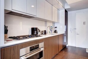 A modern kitchen with white cabinets, a built-in oven, and a coffee maker. - Modern Studio | Midtown West | by GLS (New York)