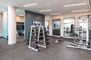 Une salle de sport moderne équipée de matériel de musculation, d’appareils de cardio et d’un écran de télévision.