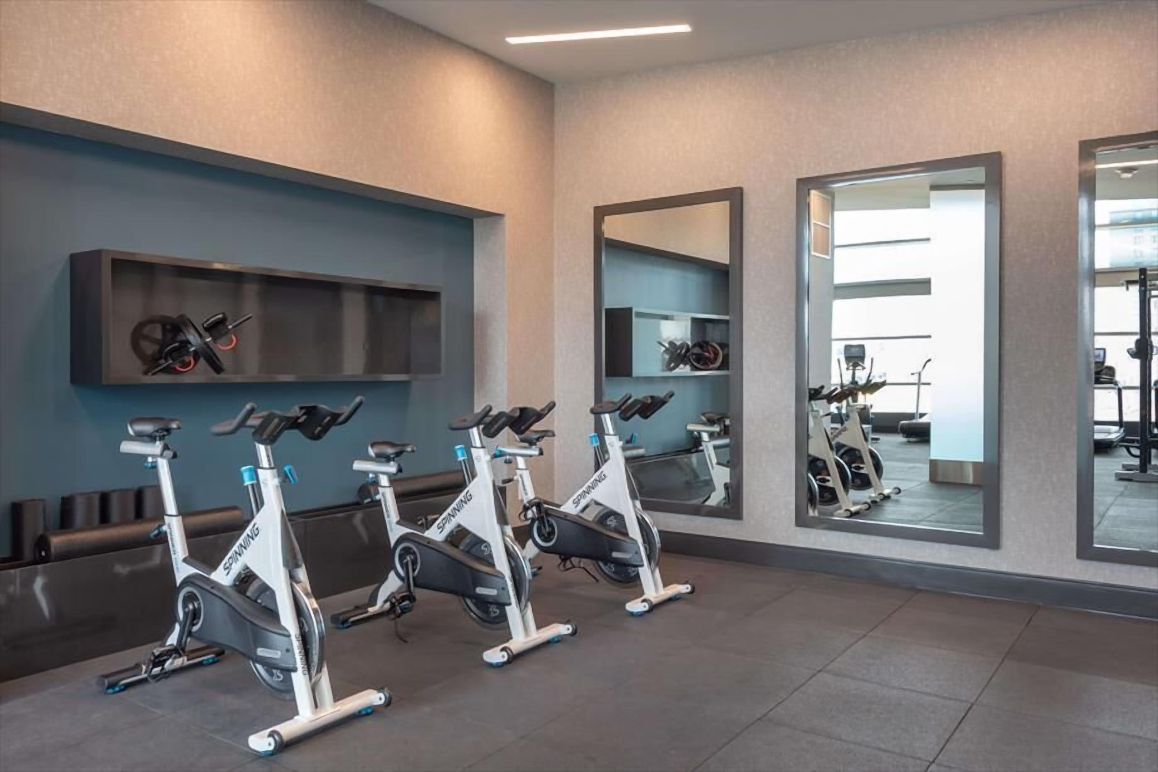 Ett gym med tre motionscyklar, ett väggmonterat ställ och speglar som reflekterar rummet.