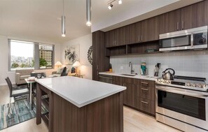 A modern kitchen with dark wood cabinets, stainless steel appliances, and a large island. - Modern 1BR | W/D | Full Kitchen | Heart of Pentagon City | GLS (Arlington)