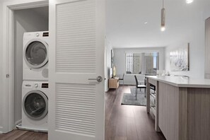 A laundry room with stacked washers and dryers, a kitchen with a wooden countertop and a dining area with a table and chairs.