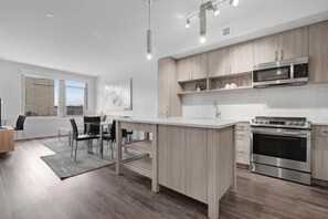 Une cuisine moderne dotée d’un îlot central, d’appareils électroménagers en acier inoxydable et de meubles de rangement en bois clair.
