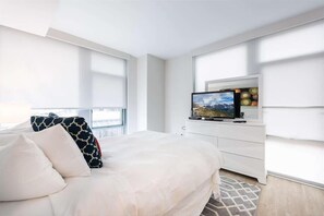 Een moderne hotelkamer met een groot bed, een flatscreen televisie en uitzicht op de stad door grote ramen.