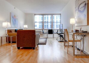 Enjoy the city view from the large window in this stylish living room, featuring a comfortable armchair, glass coffee table, and dining area with a glass table and chairs.