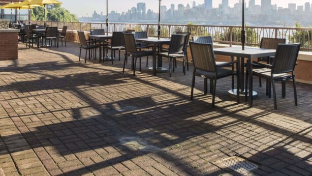 An outdoor patio with tables and chairs, yellow umbrellas, and a city skyline view.
