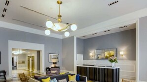 A modern living room with a sofa, coffee table, and chairs. There is a kitchen area with a counter and a wall-mounted mirror.