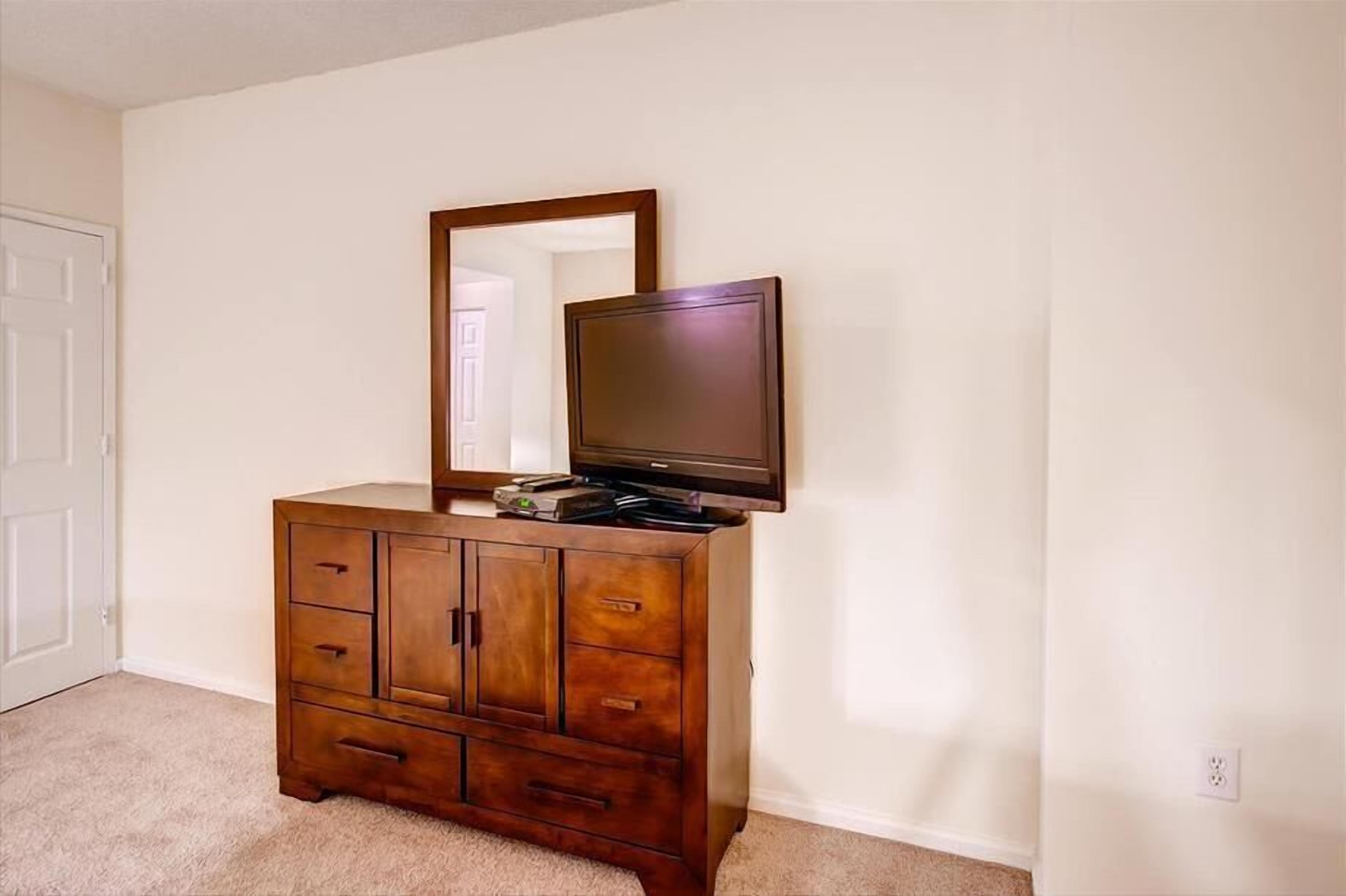 A wooden dresser with a mirror and a television.