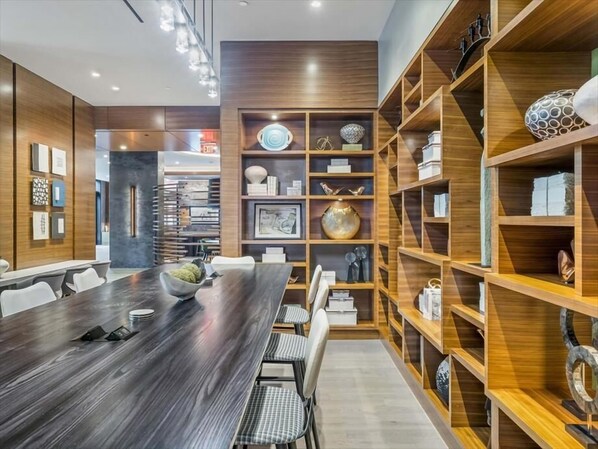 Una sala de reuniones moderna con una larga mesa de madera, sillas blancas y estanterías empotradas de madera con objetos decorativos.