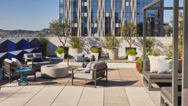 A rooftop terrace with outdoor seating, potted plants, and a view of a modern building.