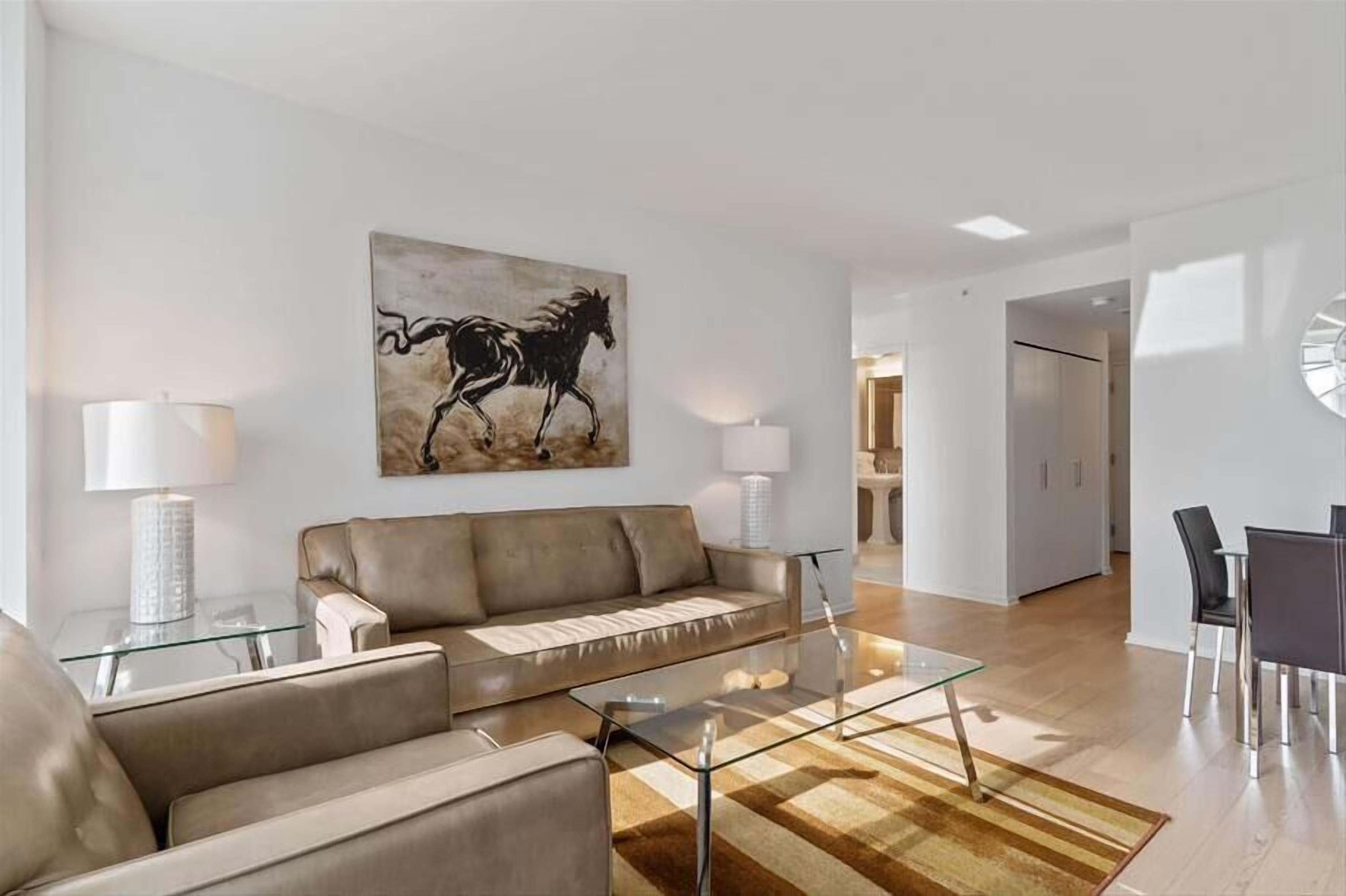 A modern living room with a sofa, glass coffee table, and a painting of a horse.