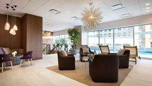 A modern hotel lobby with a seating area, large windows, and a decorative ceiling light.