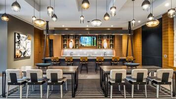 Un moderno vestíbulo de hotel con una zona de bar central, varios arreglos de asientos e iluminación colgante.
