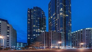 A high-rise building with a modern architectural design, featuring a prominent corner and multiple floors with illuminated windows. - Clean & Spacious 1BR | Work Remote | Free WiFi & Kitchen | Near PATH (Jersey City)