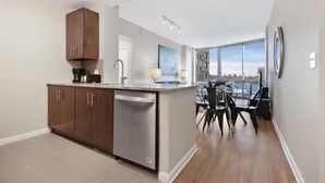 A modern kitchen with a dishwasher, a dining area with a view, and a large window. - Clean & Spacious 1BR | Work Remote | Free WiFi & Kitchen | Near PATH (Jersey City)