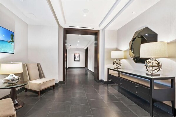 A hotel lobby with a modern design, featuring a long hallway, a seating area with a sofa and a table, and a console table with decorative items. - Clean & Spacious 1BR | Work Remote | Free WiFi & Kitchen | Near PATH (Jersey City)