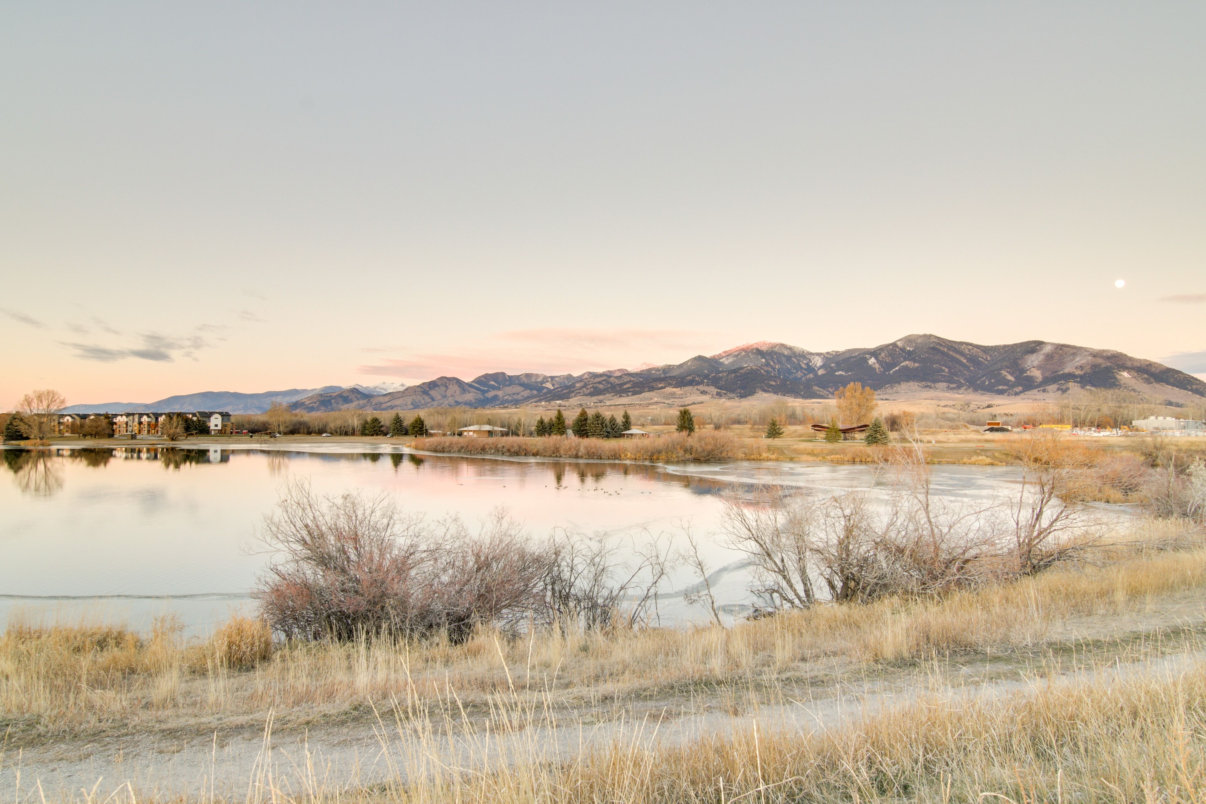 A serene landscape with a lake, mountains, and a small building in the foreground.