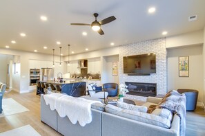 Ein modernes Wohnzimmer mit grauem Sofa, Kamin und Küchenbereich mit weißen Schränken sowie einem Esstisch.
