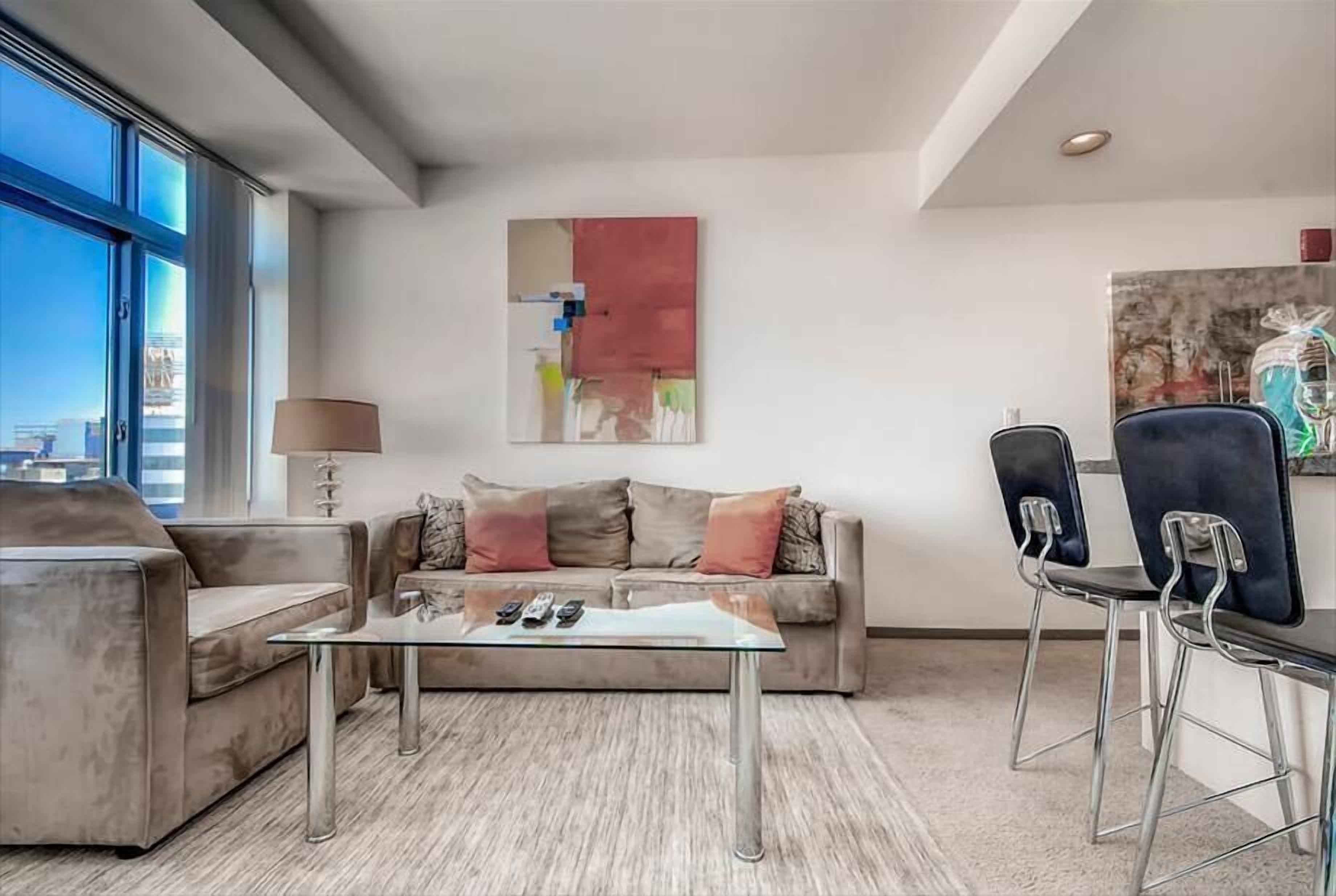 A modern living room with a sofa, a glass coffee table, and a dining area with chairs.