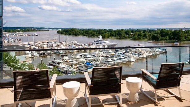 Ein Balkon mit drei Stühlen und einem Tisch mit Blick auf eine Marina, in der zahlreiche Boote liegen.