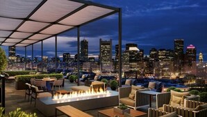 Eine Dachterrasse mit Außenbestuhlung, einem Feuerkorb und Blick auf die Stadtlandschaft.