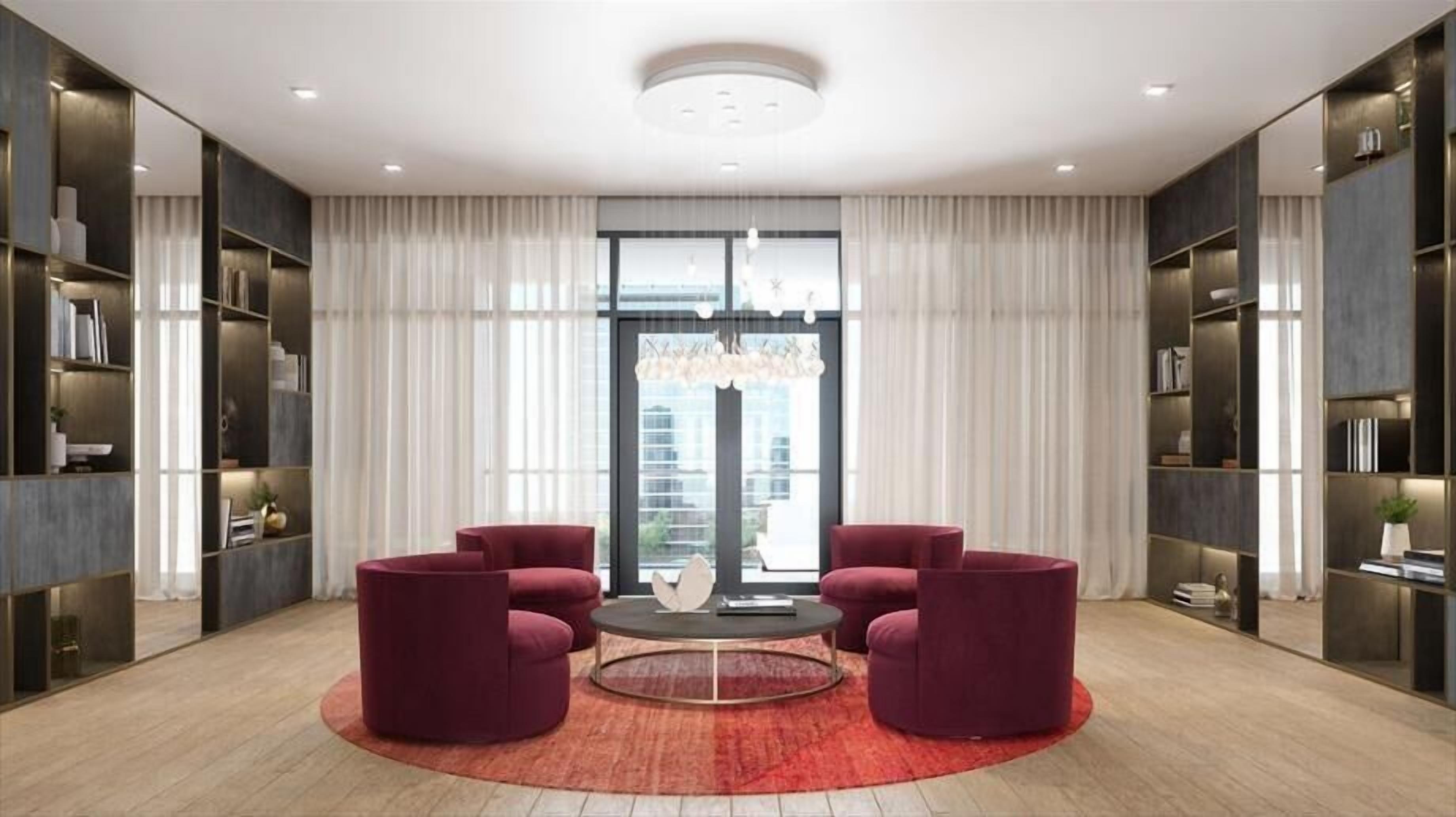 A modern living room with a round coffee table, two red armchairs, and a large window with curtains.