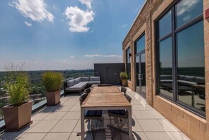 A rooftop terrace with a wooden table and chairs, potted plants, and a seating area. - Stylish 1BR | Work Space+WiFi | Pentagon City (Arlington)