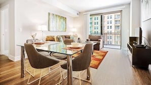 A modern apartment with a dining area, a sofa set, a TV, and a balcony with a city view.