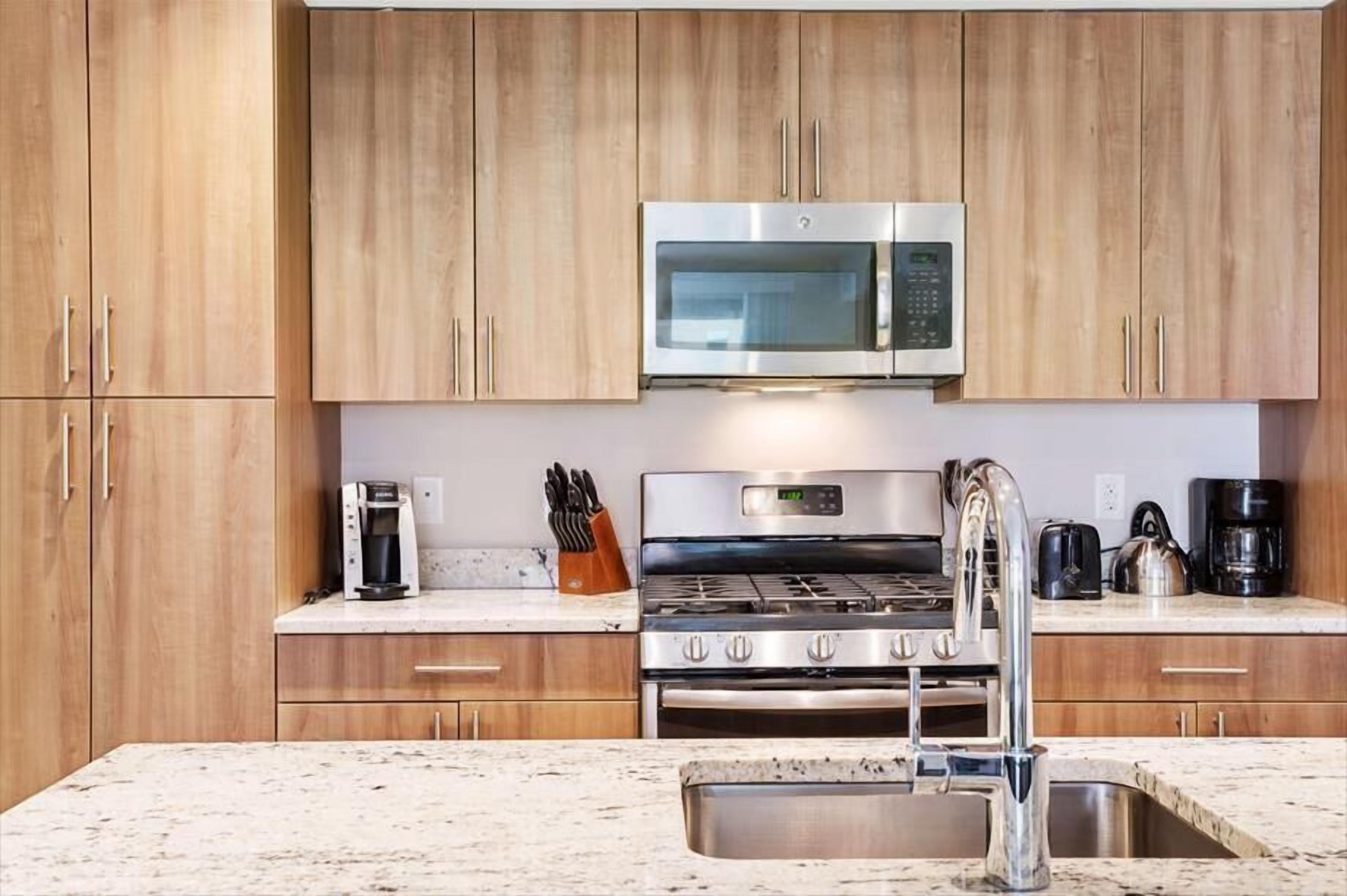 A kitchen with wooden cabinets, a stainless steel microwave, a gas stove, and a sink.