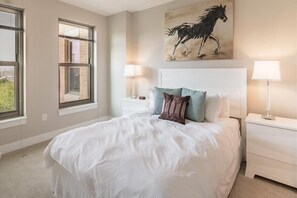 Une chambre à coucher avec un grand lit, deux tables de chevet, une fenêtre et un tableau représentant un cheval.