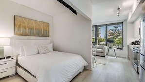 A modern bedroom with a large bed, a nightstand, a desk, and a view of the outside through a large window. - Relax in This Modern 1BR w/ Essentials & Metro Access (Washington)