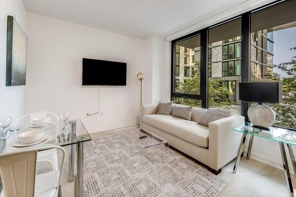 A modern living room with a sofa, glass coffee table, and a TV mounted on the wall.