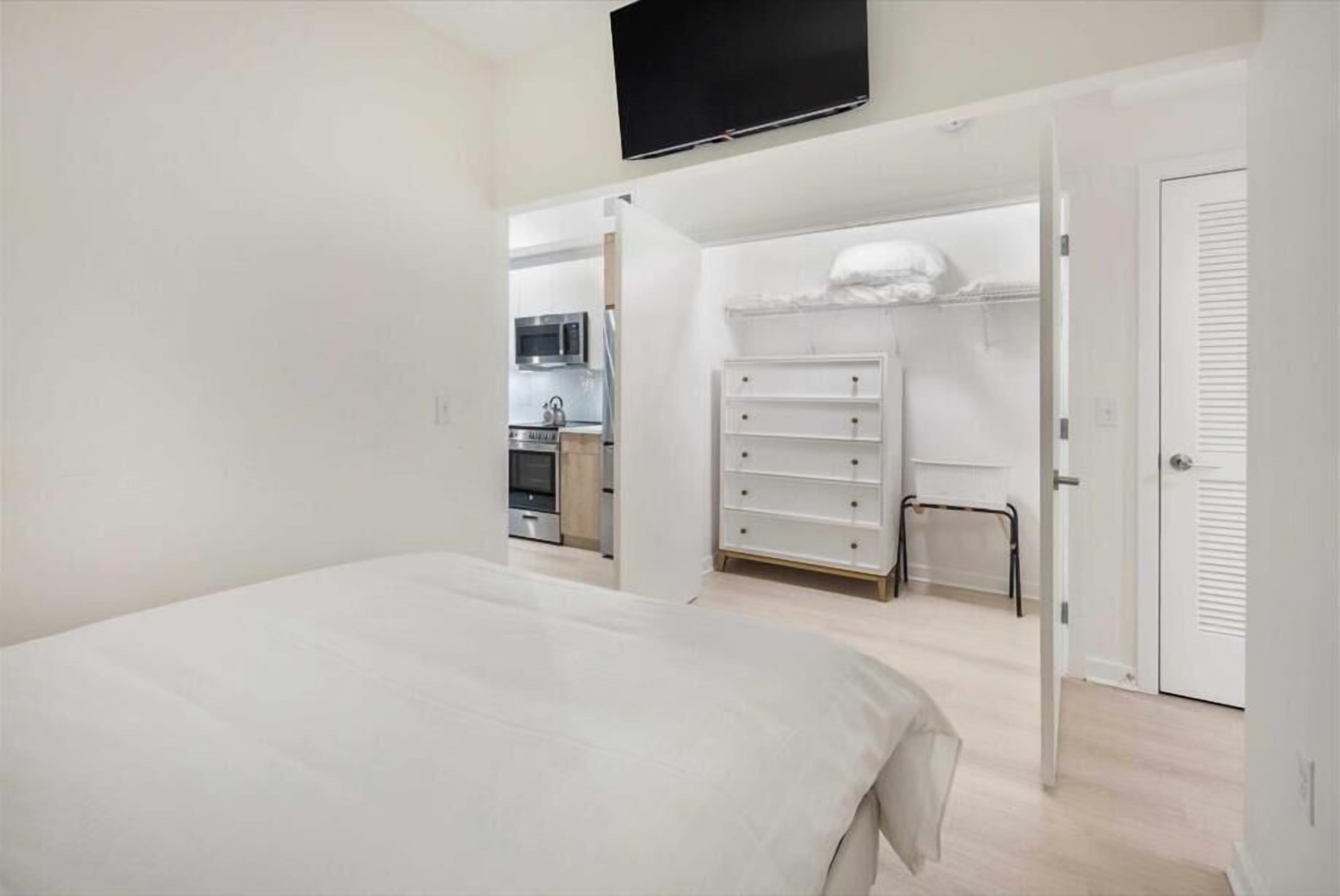 Un dormitorio con cama, televisor montado en la pared, vestidor y kitchenette.