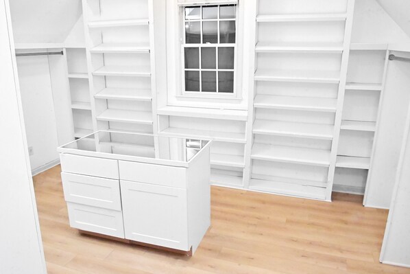 Ein weißer Schrank mit mehreren Regalen und Schubladen, einem Fenster und Holzboden.
