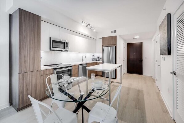 A modern kitchen with white cabinets, a stainless steel refrigerator, and a glass dining table.