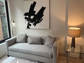 A modern living room with a grey sofa, patterned cushions, a large abstract painting, a floor lamp, and a glass coffee table.