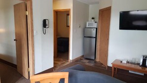 A compact hotel room with a bed, a small table, a TV, a microwave, and a refrigerator. - Pines Motel (Hinton)