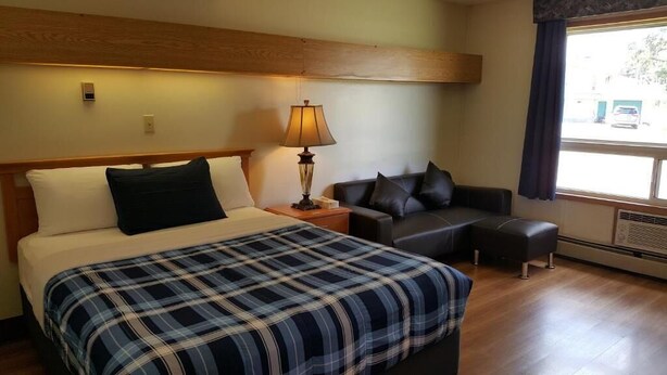 A hotel room with a bed, a nightstand, a lamp, a sofa, and a window with curtains. - Pines Motel (Hinton)