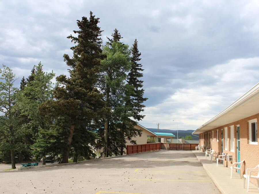 A motel with a parking lot, outdoor seating, and a row of rooms with windows.