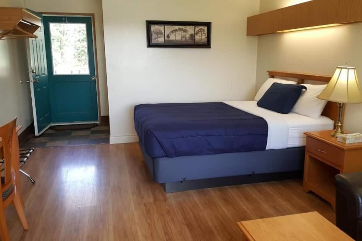Un dormitorio con cama, mesita de noche, lámpara y una puerta con vistas a árboles.