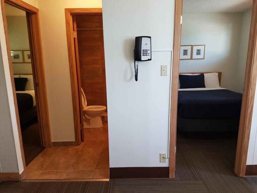 A hotel room with a wooden door, a telephone on the wall, a bed, and a framed picture.