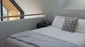 Een slaapkamer met dakraam, een bed met een gestreept kussen, een nachtkastje met een lamp en een hangende lamp.