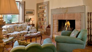 A cozy living room with a fireplace, a sofa, a bookshelf, and a dining table. - Beautiful private villa for 8 guests with A/C, WIFI, private pool, TV, patio and panoramic view (Montelopio)