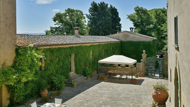 A courtyard with a stone floor, a table with chairs, a covered outdoor seating area, and a building with a tiled roof partially covered by ivy. - Beautiful private villa for 8 guests with A/C, WIFI, private pool, TV, patio and panoramic view (Montelopio)