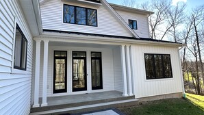 Ein zweigeschossiges Haus mit Veranda, großen Fenstern und einem gepflegten Rasen.
