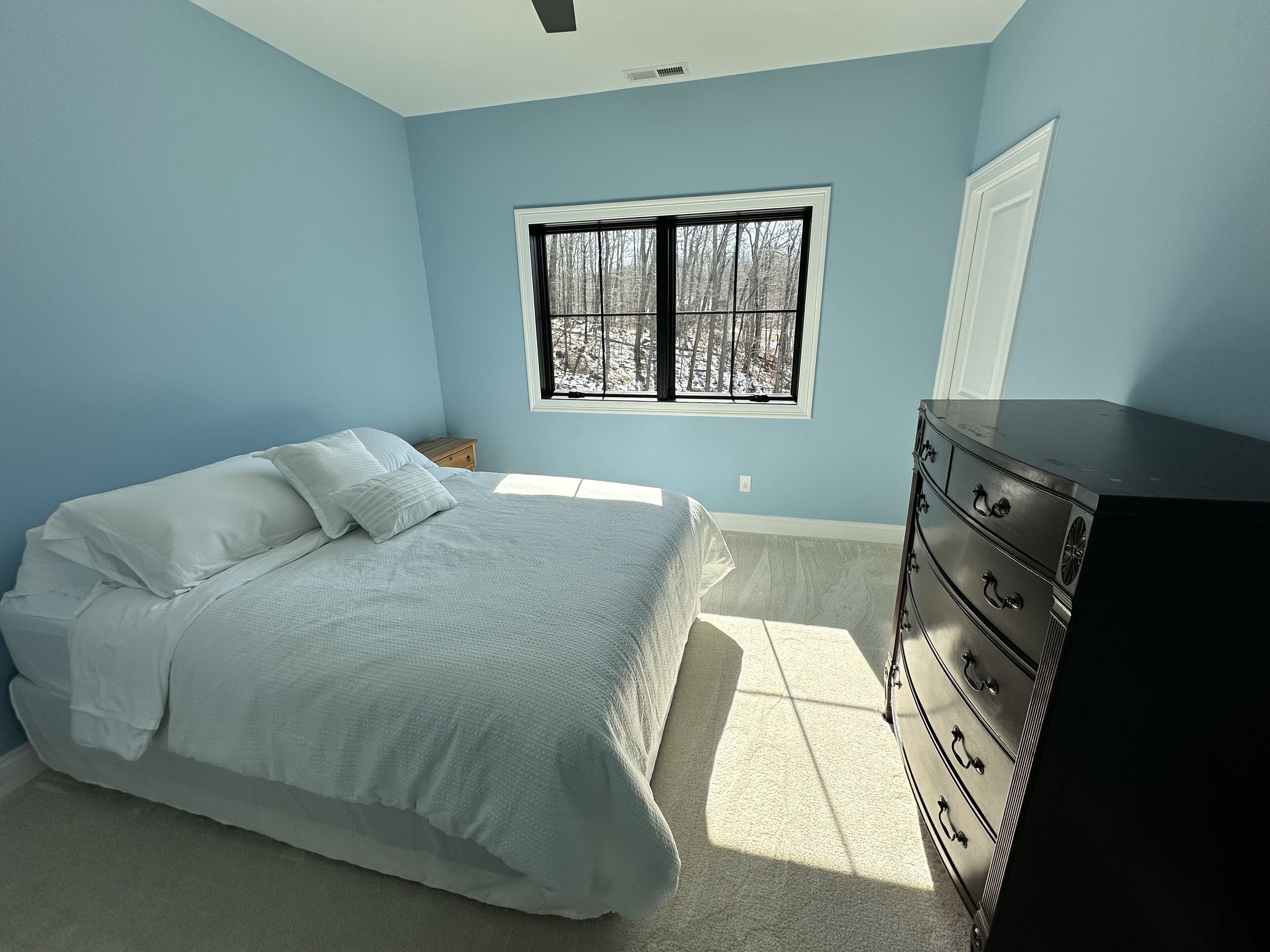 Une chambre à coucher avec un lit, une commode et une fenêtre donnant sur des arbres.
