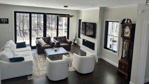 Ein geräumiges Wohnzimmer mit großem Fenster, Kamin, einer Uhr und einem Sofa.