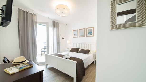 A hotel room with a bed, a desk with a hat and a book, a TV, and a window with curtains.